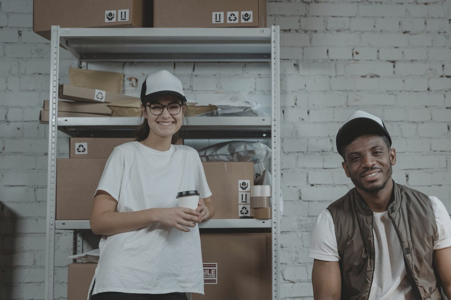 Two dispatch office staff at a desk with parcels on the shelves behind them, both smiling